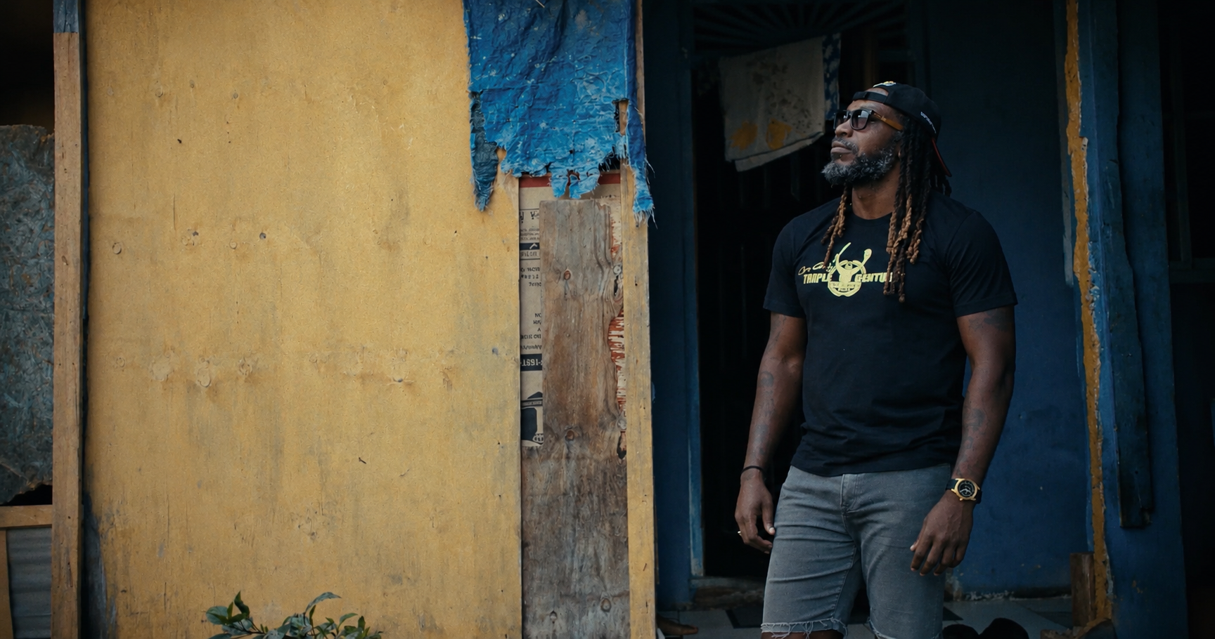 Chris Gayle stands in the doorway of a weathered yellow and blue house.