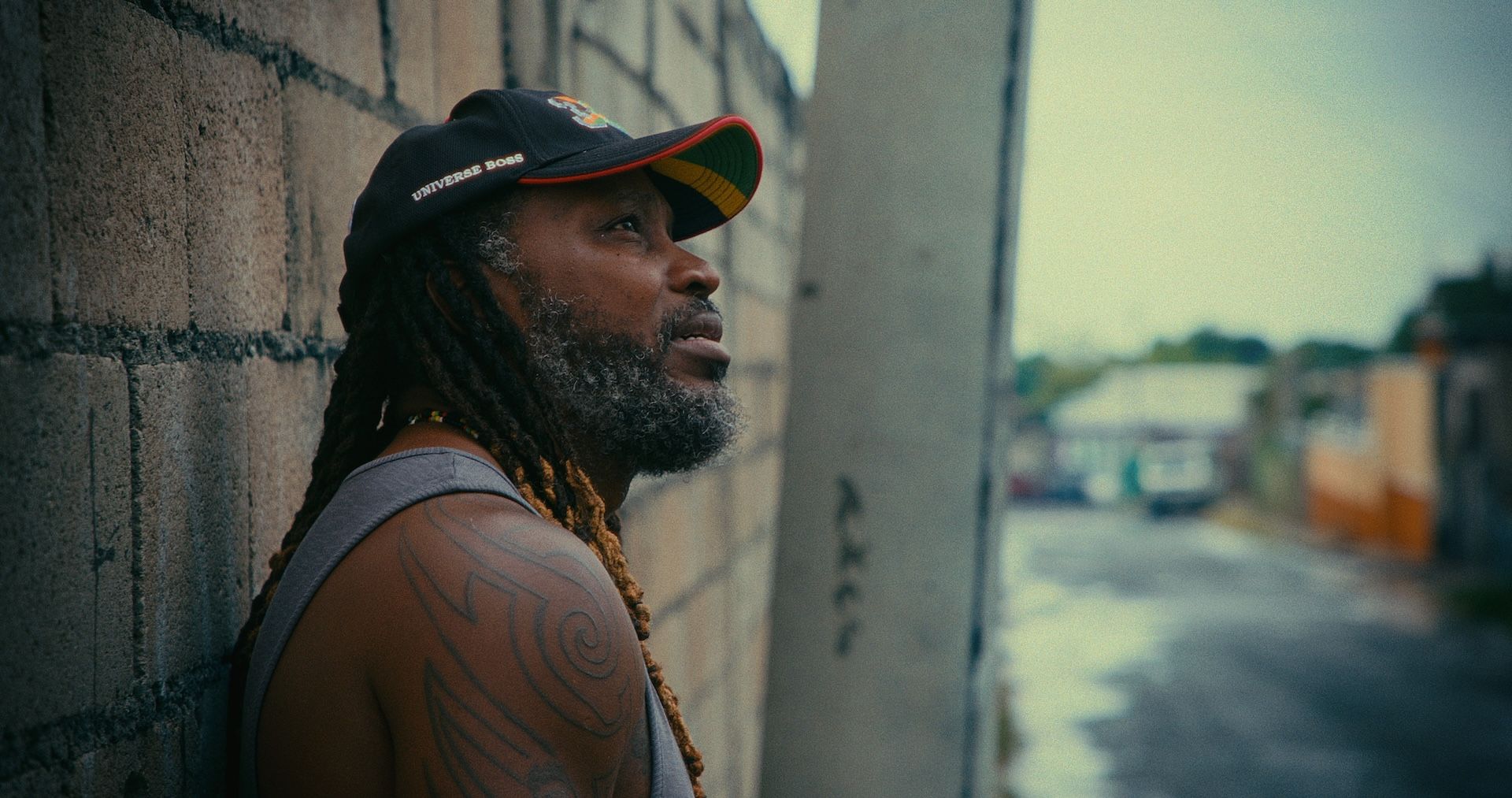 Chris Gayle leans against a block wall, looking up the street.