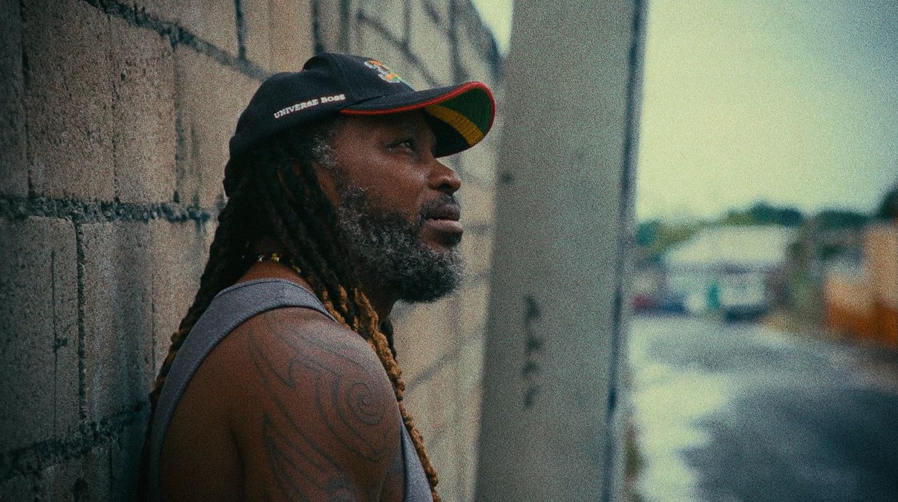 Chris Gayle leans against a block wall, looking up the street.