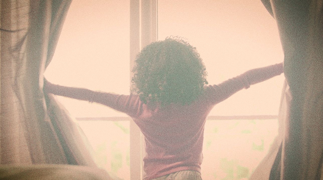 A child throws open curtains to a bright window.